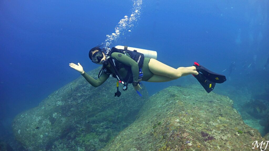 Female scuba diver floating comfortably underwater at a rocky reef in Phuket.
